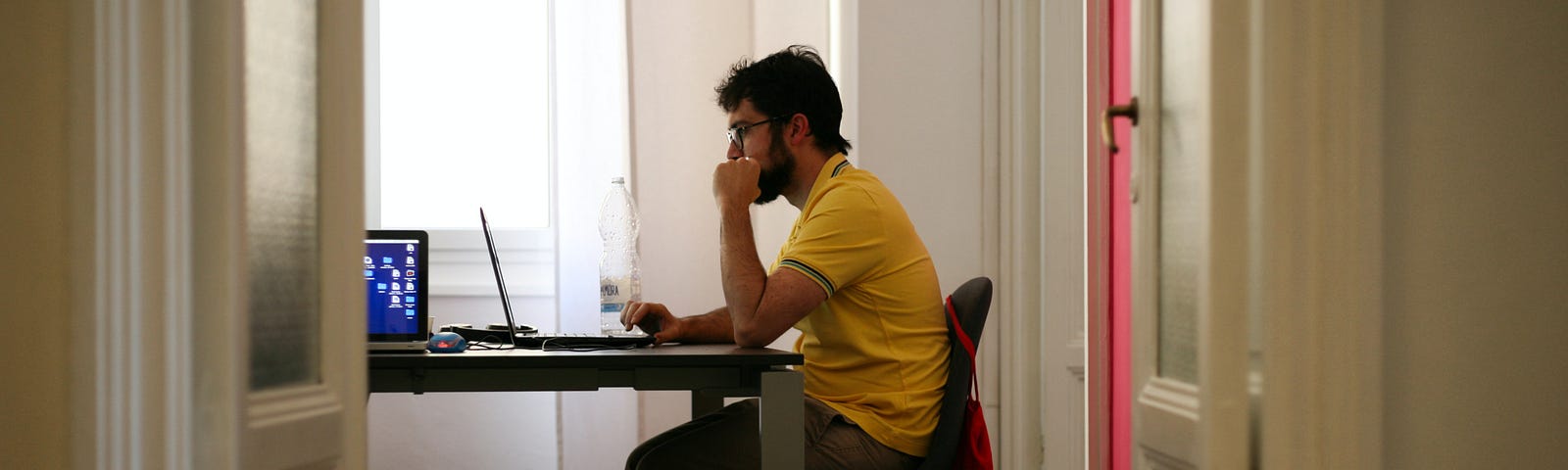 Man in yellow shirt sitting at a table, typing on laptop computer