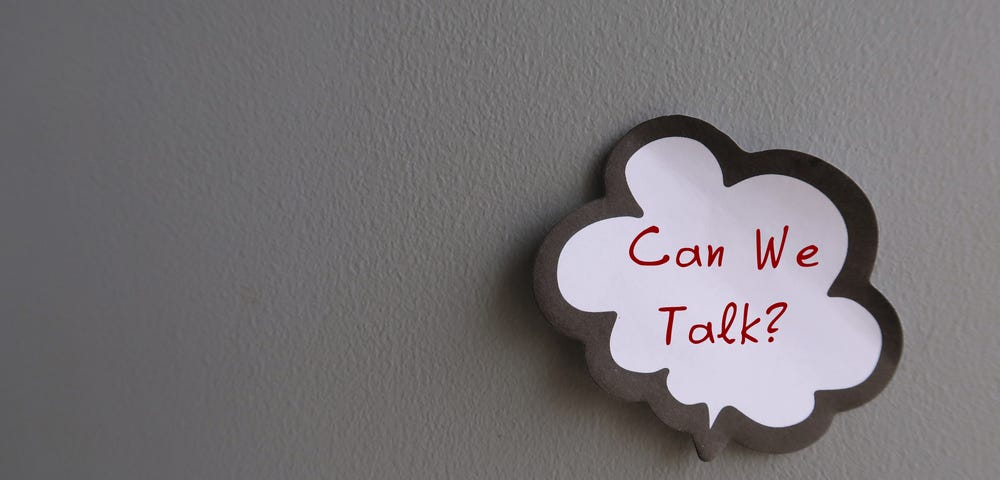 A wall with a sticker on it, saying “Can we talk?”