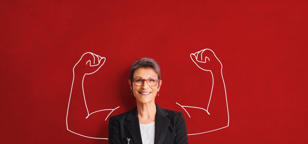 A woman wearing glasses and a dark suit coat over a white blouse. she is smiling with her arms crossed. behind her is a red background and a drawing in white of two large muscular arms, as if they werebpart of her. The image is intended to portray inner strength.