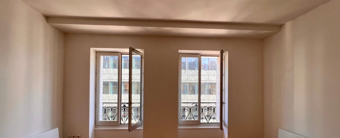 An empty apartment with two traditional French windows and a hardwood floor.