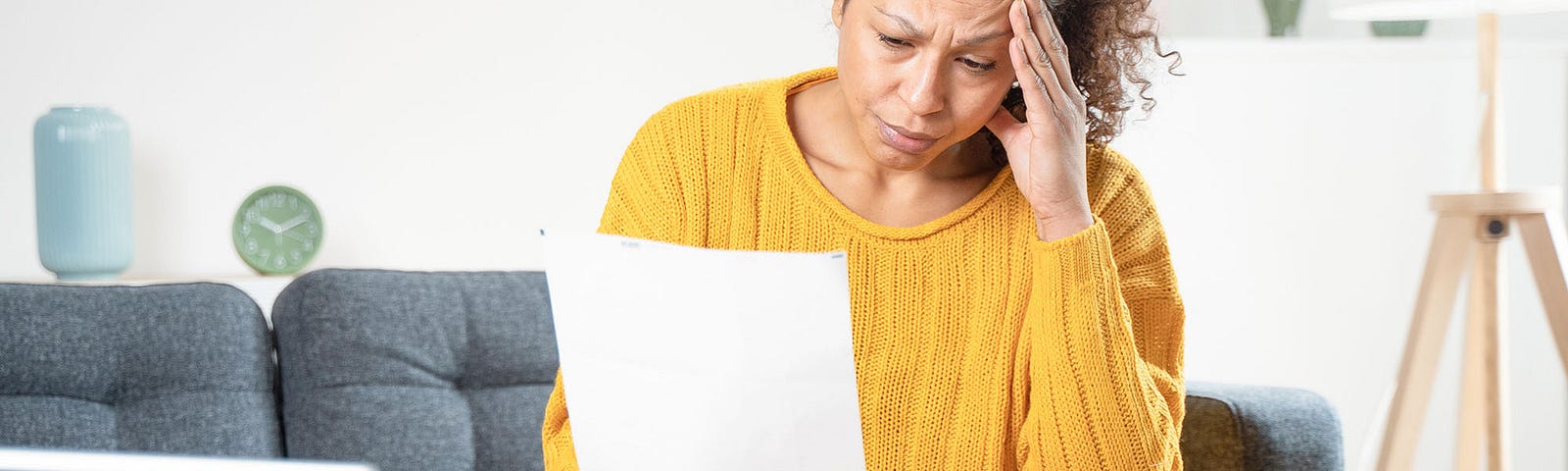 Middle-aged woman looking at a bill in her hand in front of a computer looking frustrated