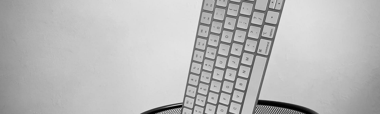 Black and white image of a hand holding an Apple Magic Keyboard with Touch ID over the trash can.