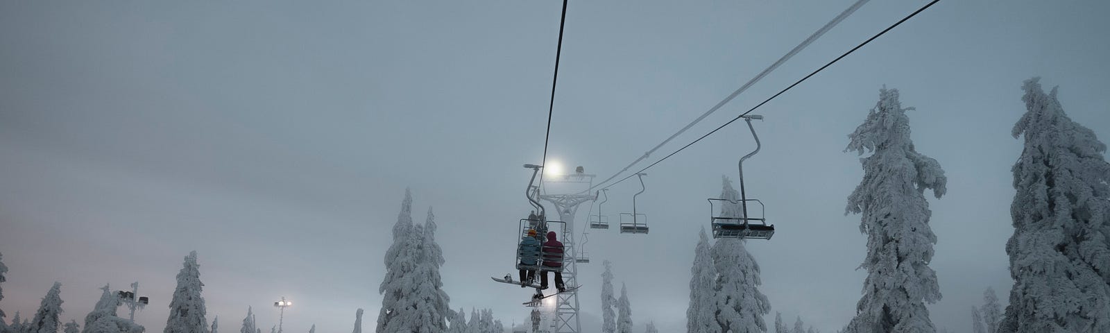 Backs of two skiers on chairlift facing light of the moon