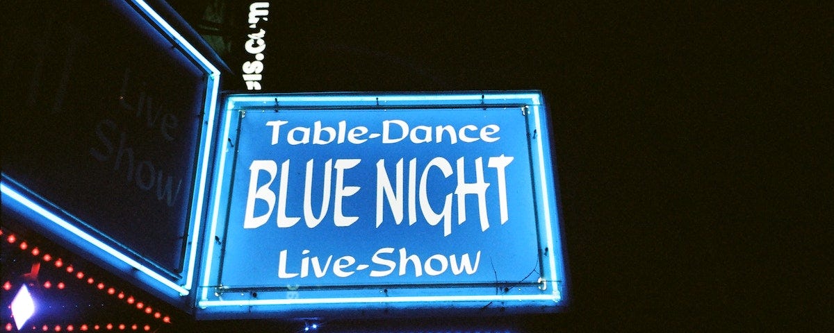 A neon sign outside a lap dancing club, advertising table dances , live shows, and ‘sexy sexy girls’.
