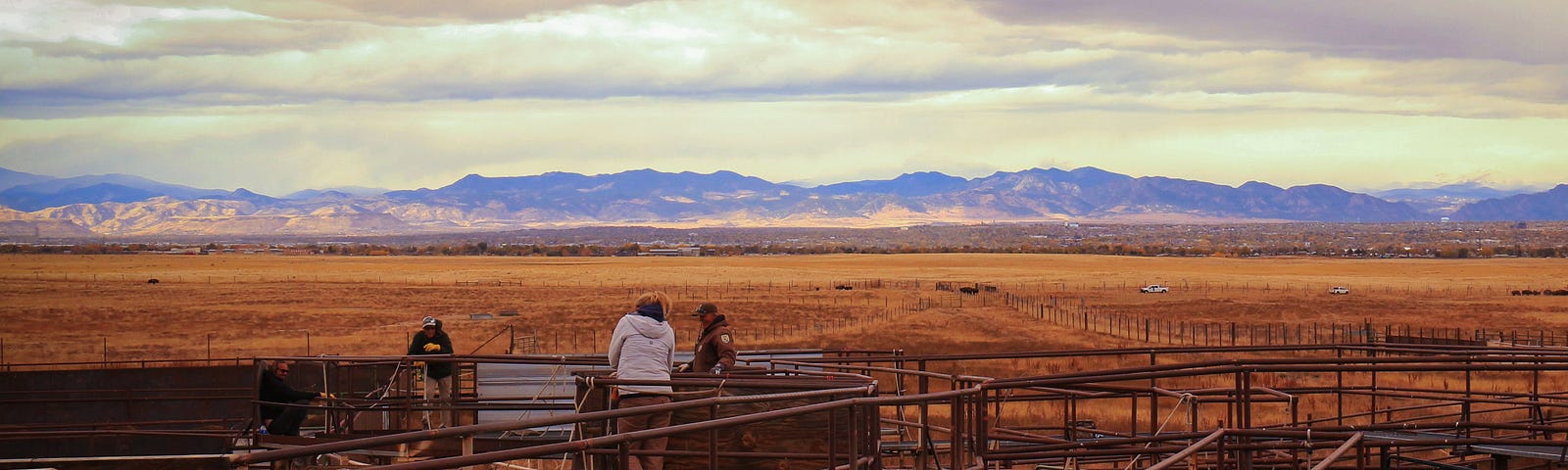 people stand on a corral in front of the Rocky Mountains mountain range