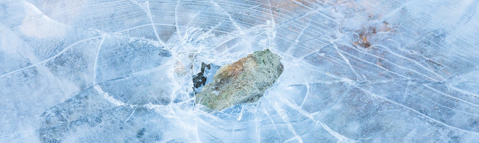 A rock breaking the ice on a frozen lake. This picture descriptive of the phrase “Ice Breaker”.