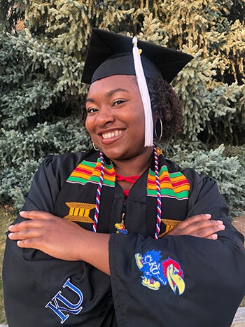 Jalynn Tann is pictured in her graduation cap and gown with her arms folded in front of a tree