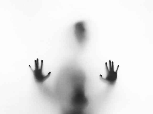 An image of a person’s silhouette with their hands pressed against foggy glass as if stuck behind a veil.