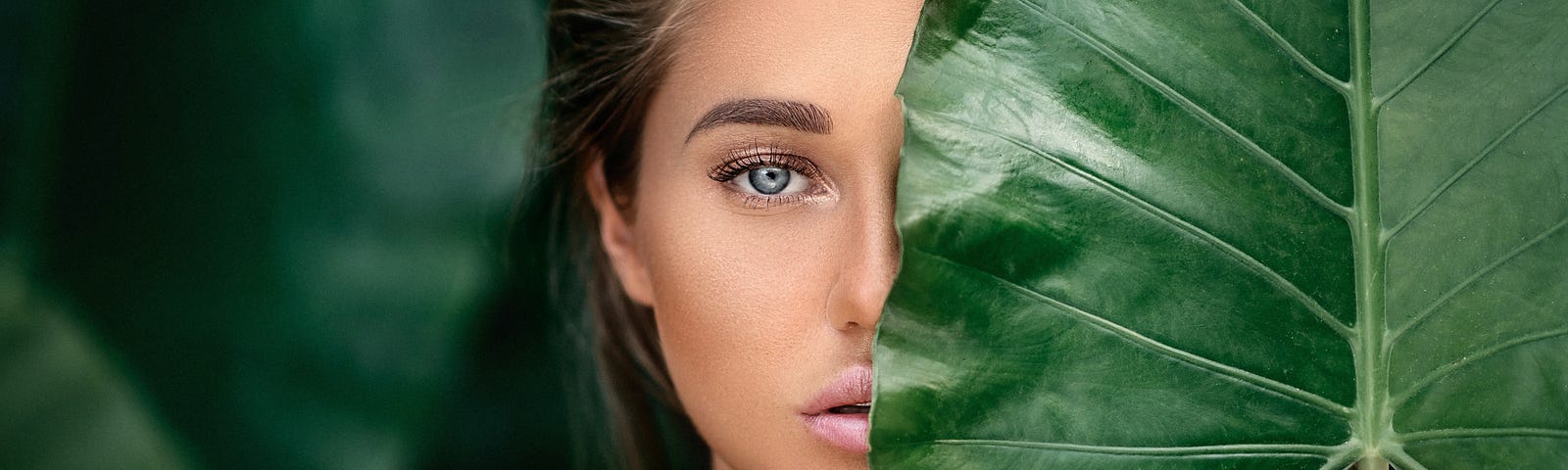 luxury-portrait-beautiful-young-woman-with-natural-makeup-holds-big-green-leaf-blurred-green — Un Swede