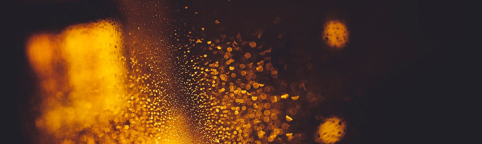 An orange light reflects off a rain streaked windshield at night.