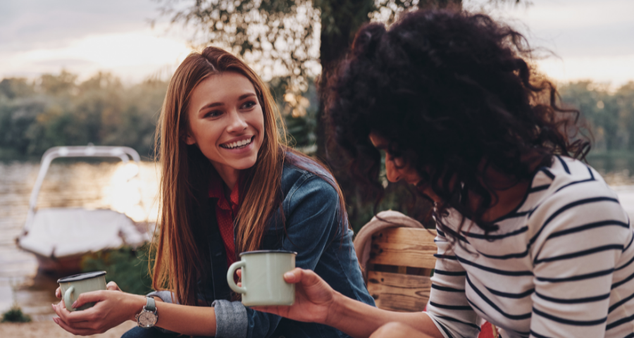 Two women smiling drinking coffee and talking outdoors