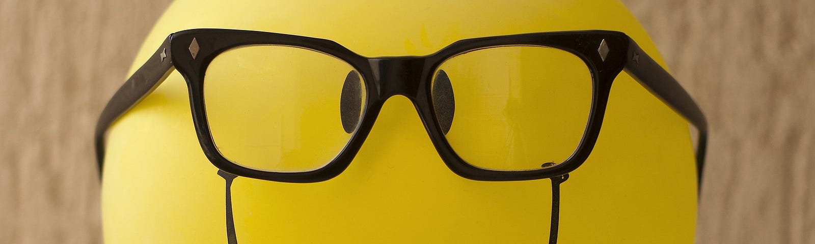 A yellow balloon with eyes and nose drawn on with marker and a pair of real glasses.