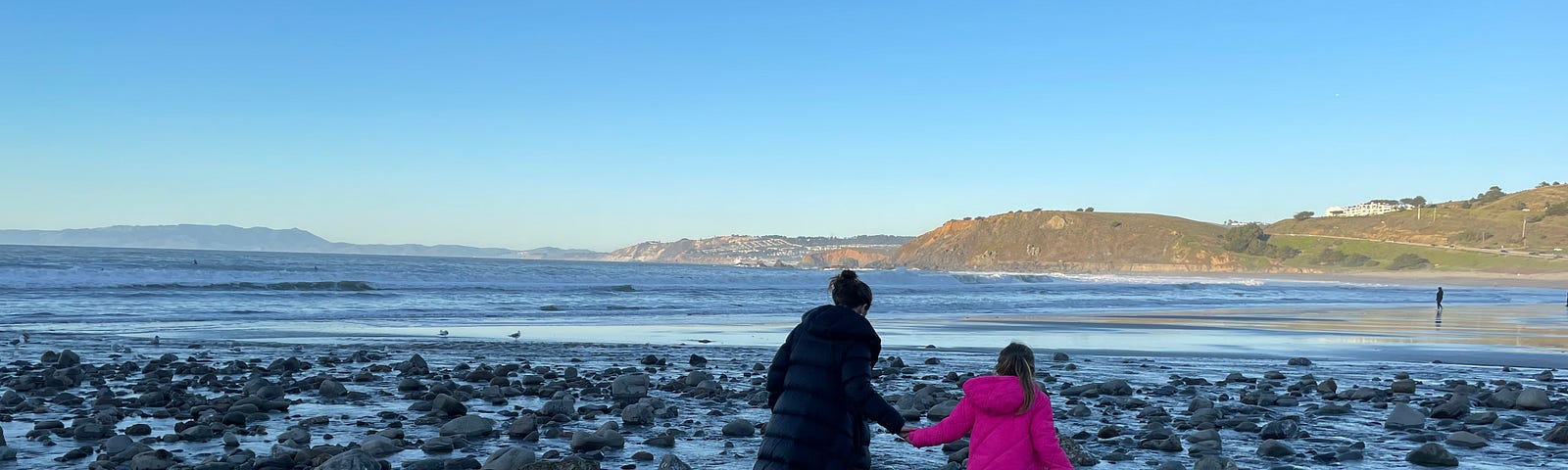 My wife holds my daughter’s hand as they traverse random rocks in the low-tide surf of Pacifica State Park Beach.