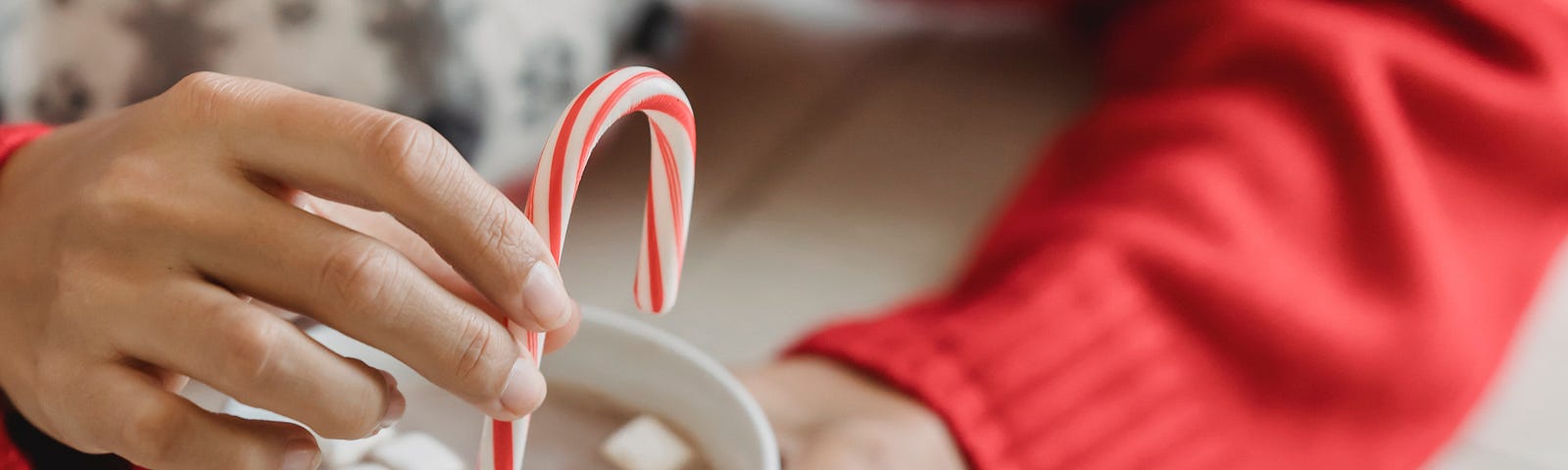 Picture of woman in sweater stirring hot chocolate with candy cane.