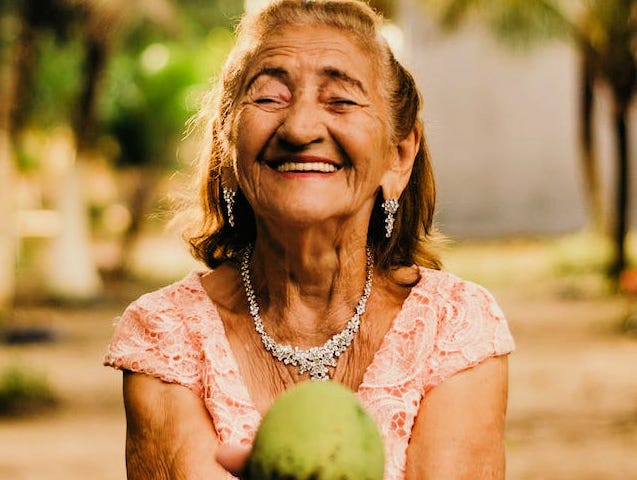 An older woman with her eyes closed, smiling, and holding a piece of fruit.