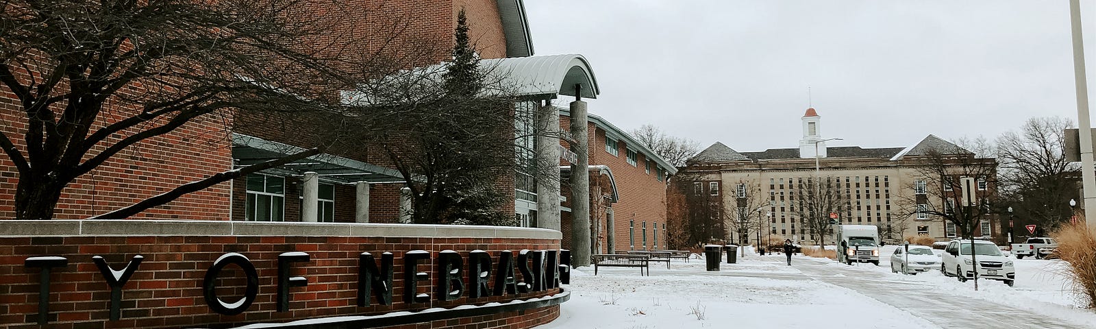 Snow covers the ground surrounding the Visitors Center with Love Library in the distance.