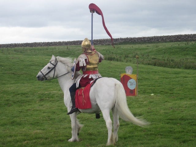 a knight on a white horse in an open green field or pasture.