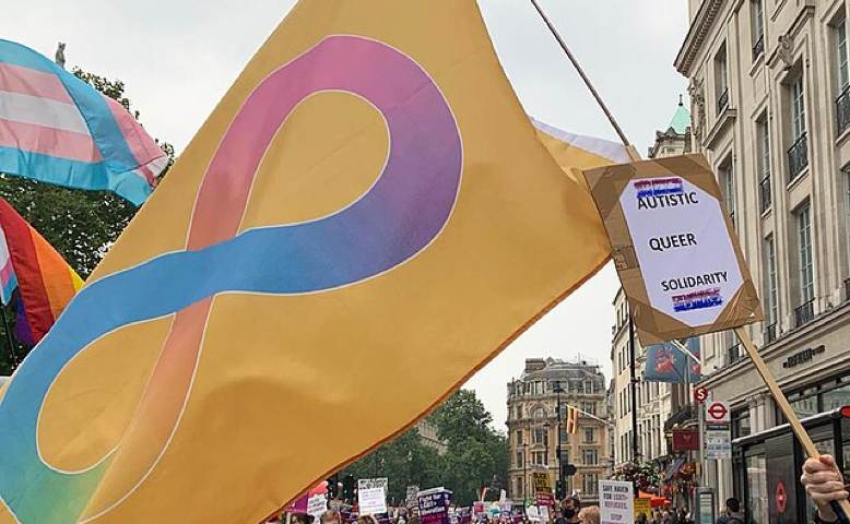 Autistic Pride Flag at Pride. Gold is used by autistic advocates as the chemical symbol for gold is Au. The infinity symbol represents the broad and varied spectrum of experiences within neurodiversity, the rainbow represents the pride movement.