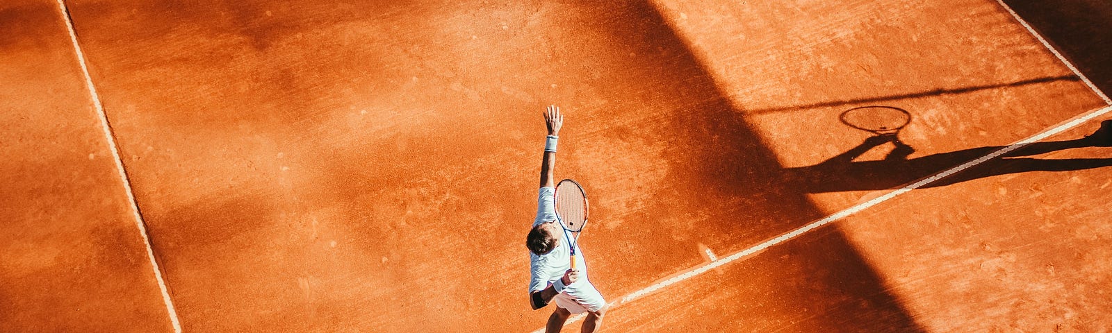 A person playing tennis on an orange court.