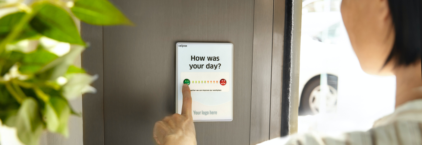 A person is interacting with a touch screen on a wall, on the screen there’s a question “how was your day?” and a scale from a smiling face to a frowning face
