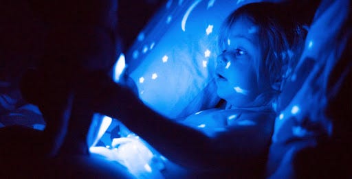 Little girl in bed at night, holding a device, which emits blue light.