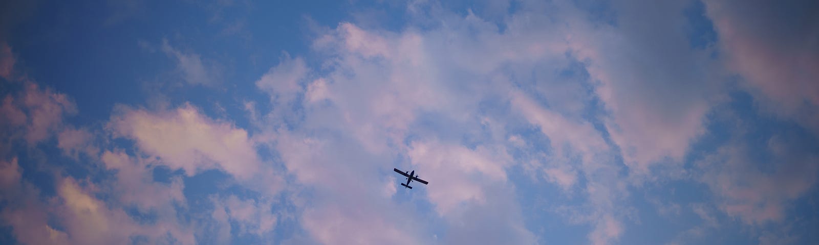 An airplane flying low, behind a fluffy fragmented cloud refracts the orange of the sunset making a contrast of the intense blue in the sky. Un aeroplano volando, detrás una nube acolchonada pero fragmentada refracta la luz del atardecer contrastando con el intenso azul en el cielo.