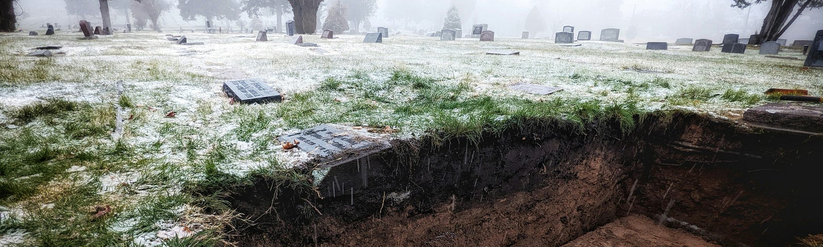 A snow covered field with an old casket in an open grave