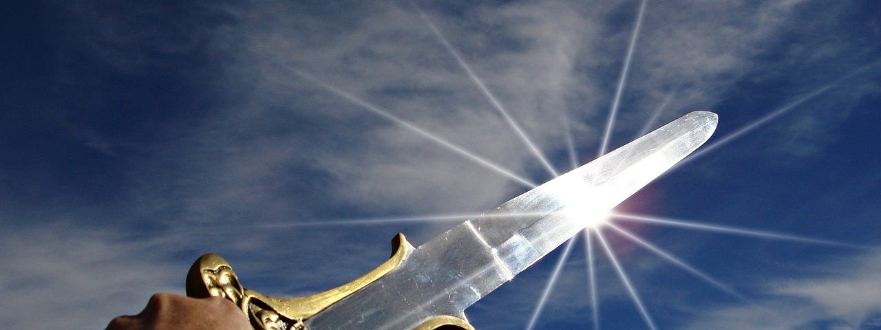 Man’s hand holding a sword against a partly cloudy blue sky, with a glint of sunlight sparking off the blade.