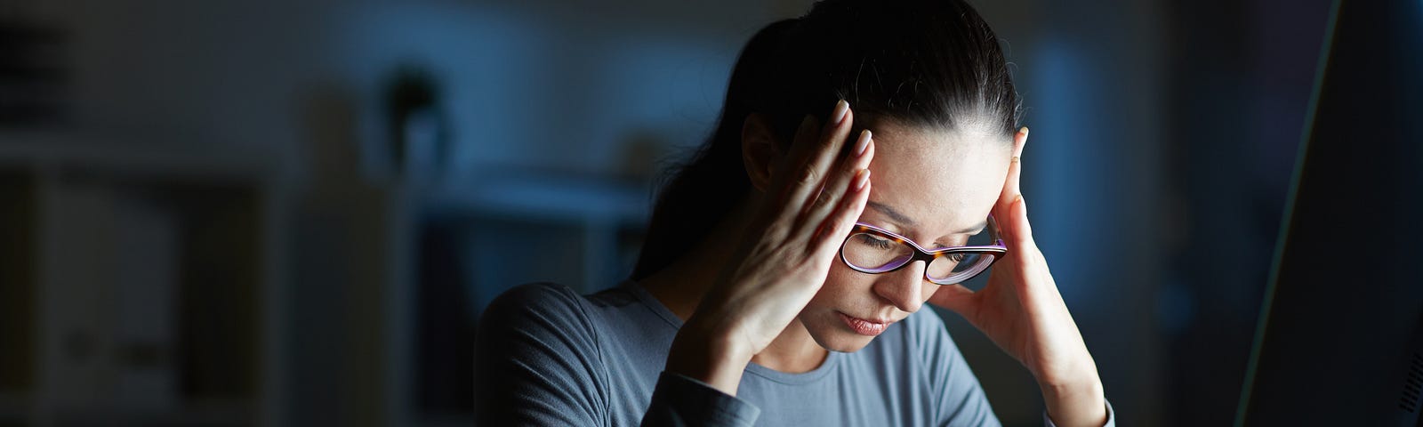 woman with glasses and long sleeves shirt, stressed in front of computer in night lighting