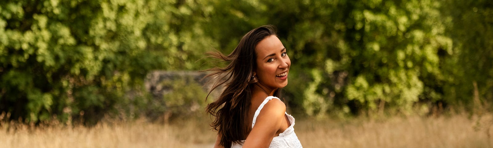 Young woman in white dress running and looking behind at camera laughing