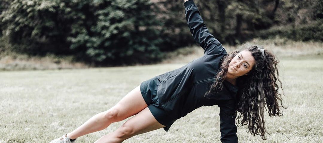 A young woman doing a side plank exercise in a grassy field.