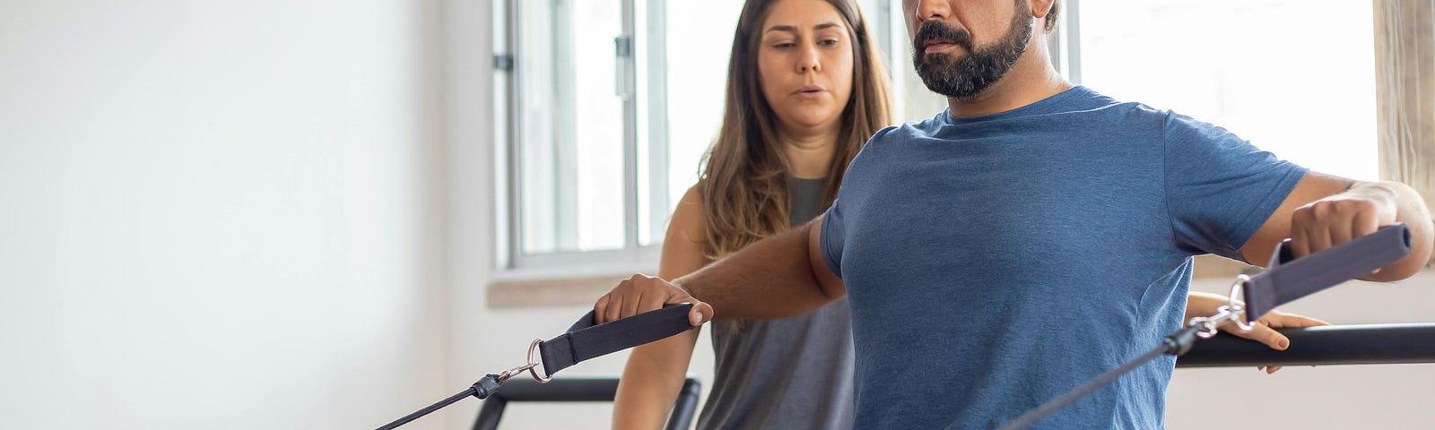 Man doing exercises on a piece of gym equipment with a female trainer standing behind him.