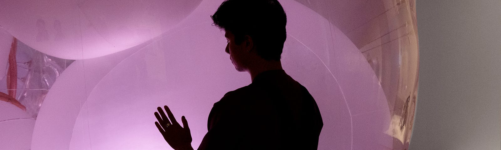 Silhouette of museum patron with one hand touching a giant, glowing pink orb.