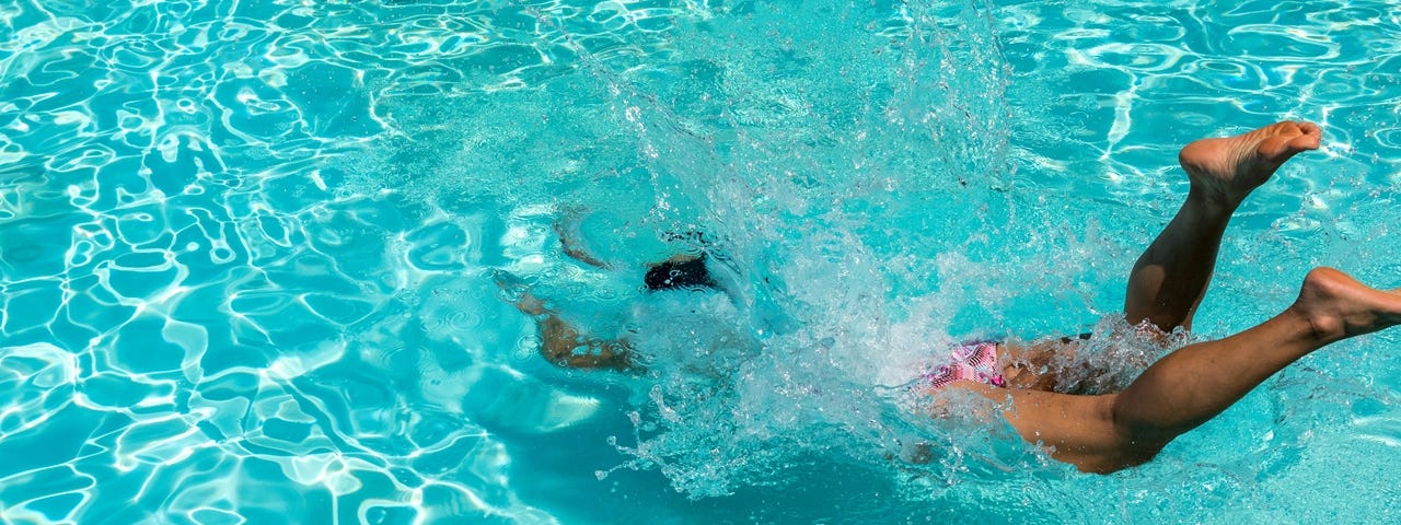 A person diving into a pool in front of a no diving sign