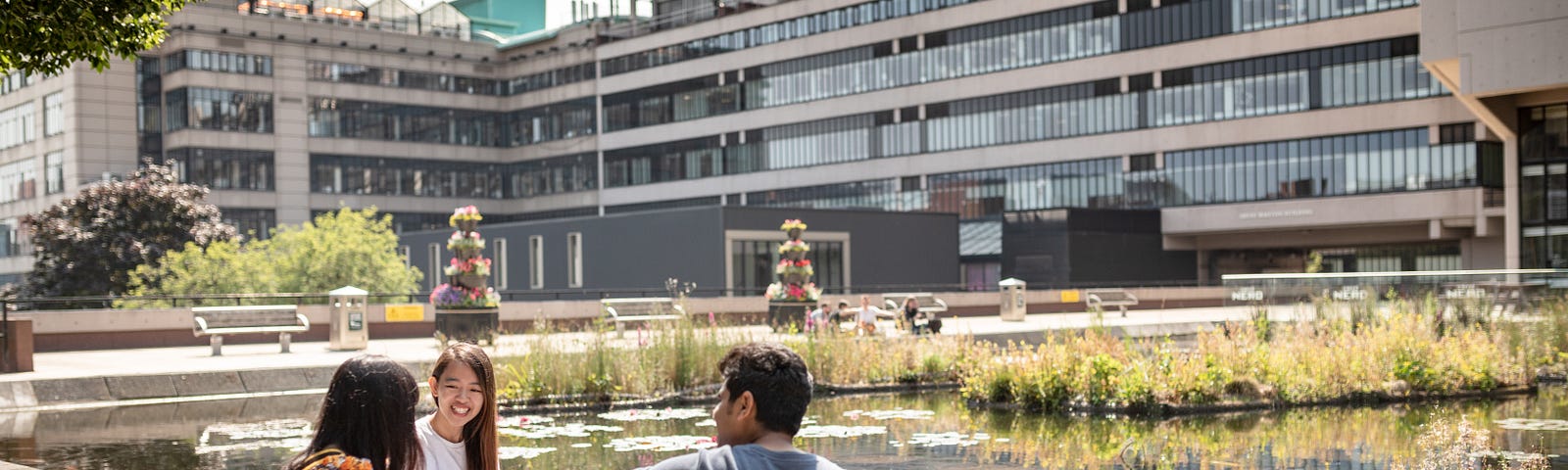 Three students sat near the large pond next to the Roger Stevens building on the University of Leeds campus.