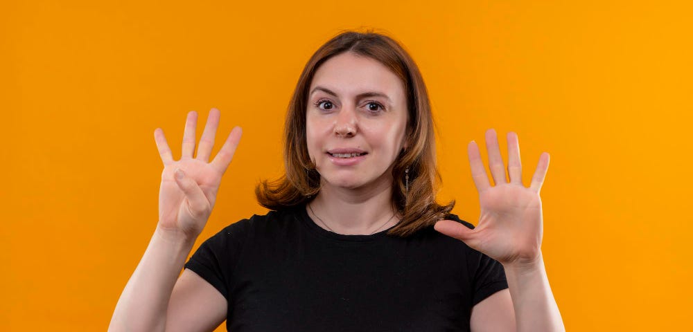 Woman with shoulder-length hair holding up nine fingers. Background is mustard yellow.