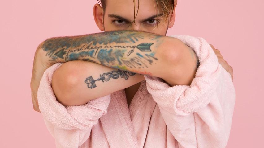 A sexy tattooed man dressed in a pink dressing gown.