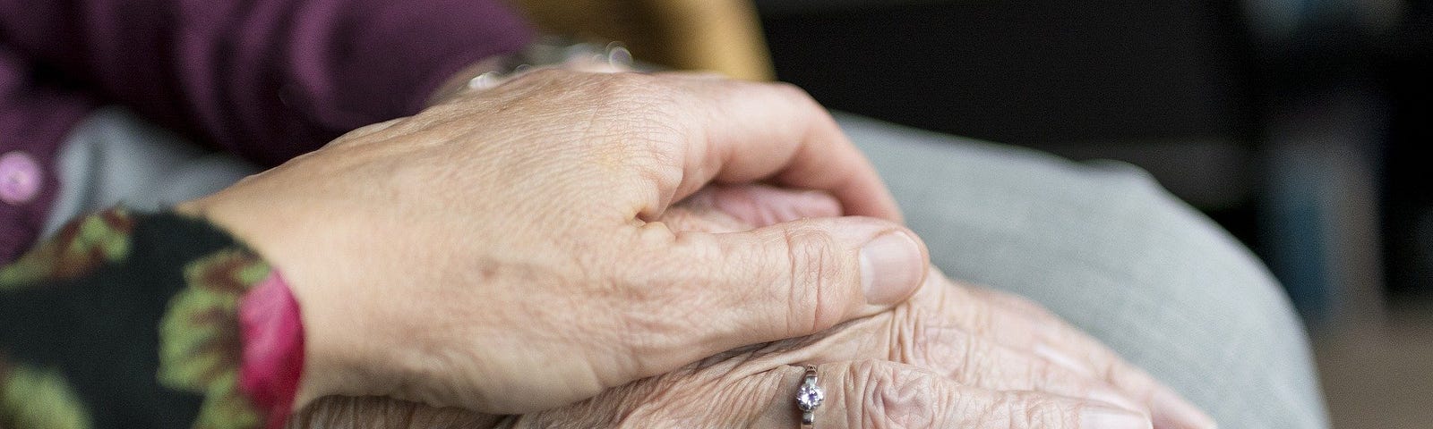 A woman’s hand covers the wrinkled hand of her elderly mother.