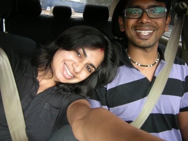 An Indian woman and Man, sitting in a car with seatbelts on. They are smiling at the camera.