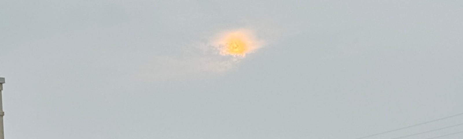 Photo of a faint sun peeking out from gray clouds.