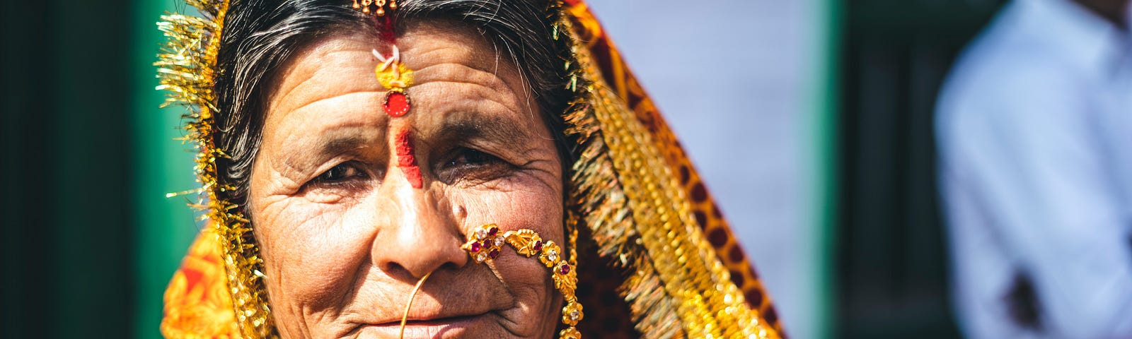 An older woman wearing a large nose-ring, shawl over her head, and a lot of colorful jewelry.