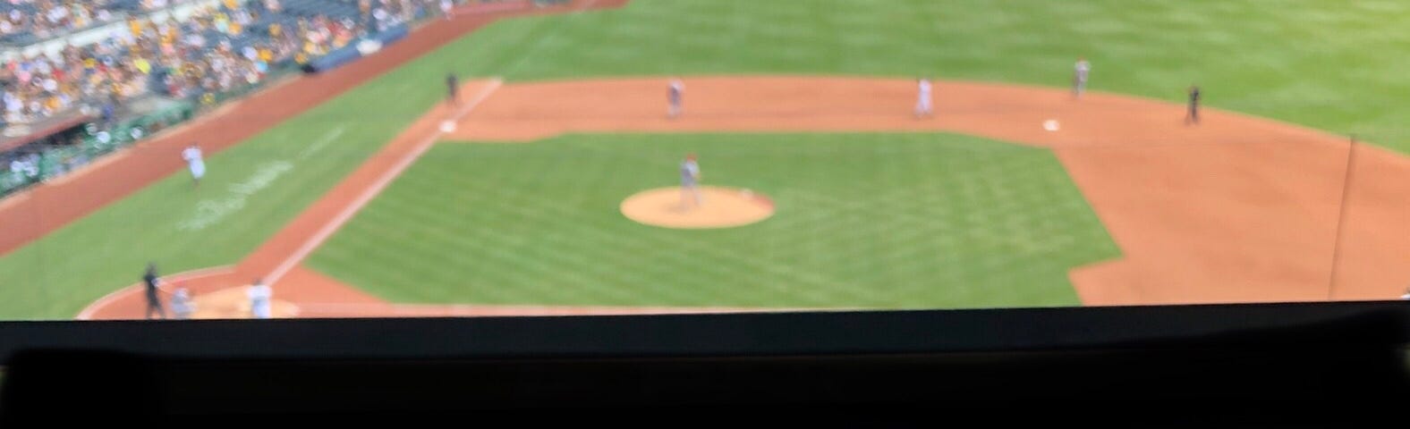 A tart packed with strawberries, blueberries, and blackberries sits on a ledge that overlooks a baseball stadium’s stands and field, with a game in progress