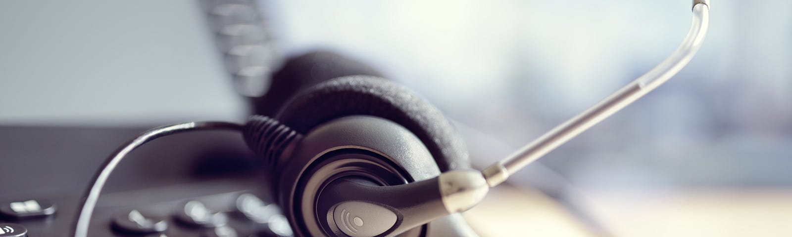 A close up of a headset resting against a black telephone.