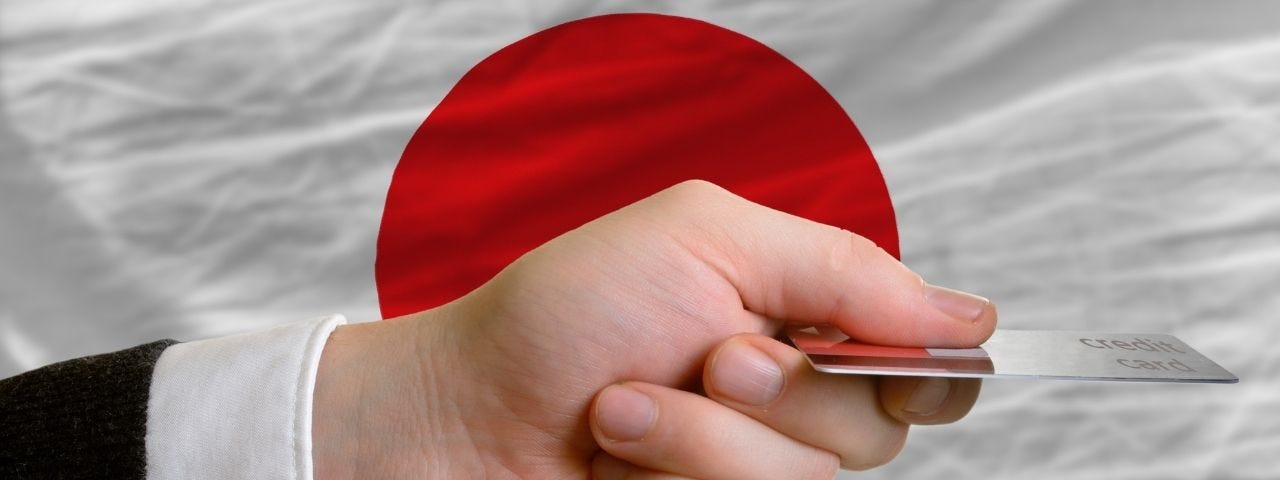 Hand presenting credit card over a flag of Japan.