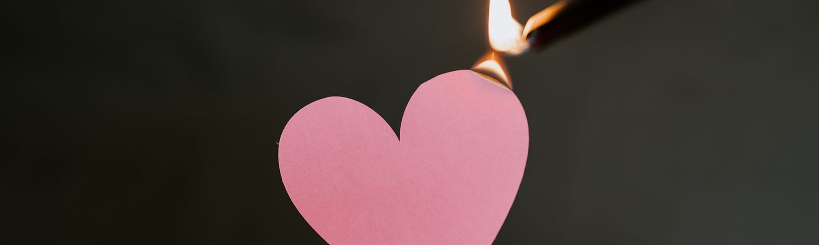 A person holding a pink heart-shaped paper as it slowly lit on fire with a lighter