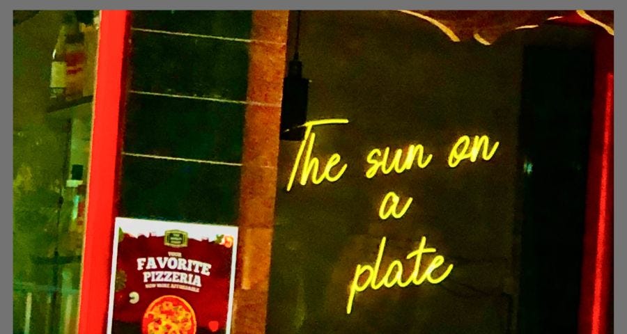 street photograph of a neon sign : the sun on a plate, taken from a Pizza joint