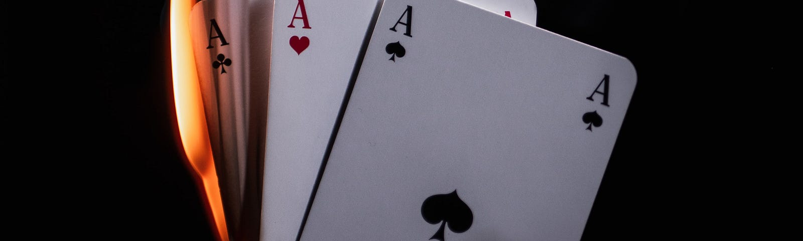 A collection of burning poker cards, showing aces, float in the air over an open hand.