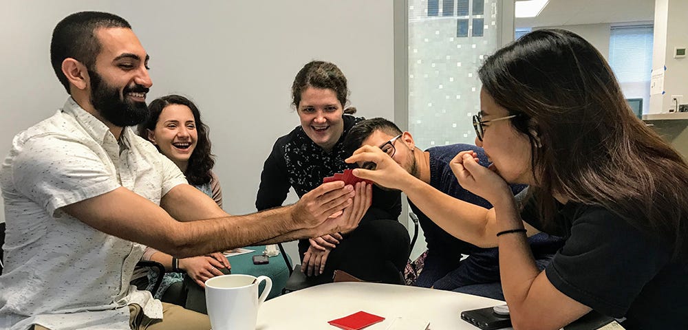 Multi-ethnic group of grad students (3 women, 2 men) play a card game.