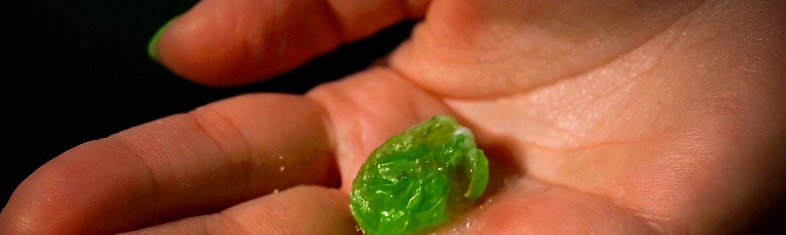 Close-up of a hand holding a lime green, misshapen gummy candy.