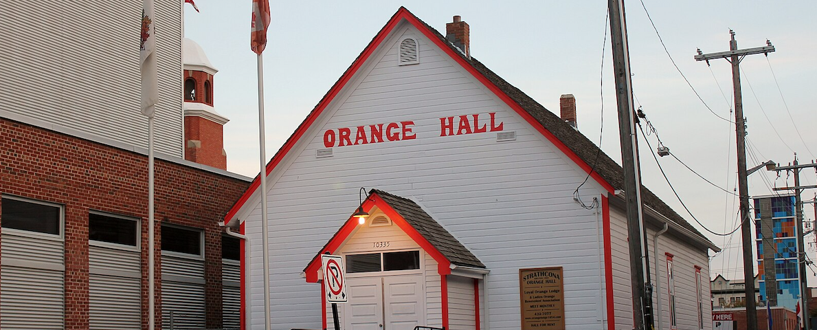 An old-fashioned white clapboard wooden hall with the name Orange Hall written above the door in orange letters.